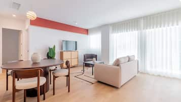 Una sala de estar moderna con comedor, sofá, televisor y un gran ventanal con cortinas.