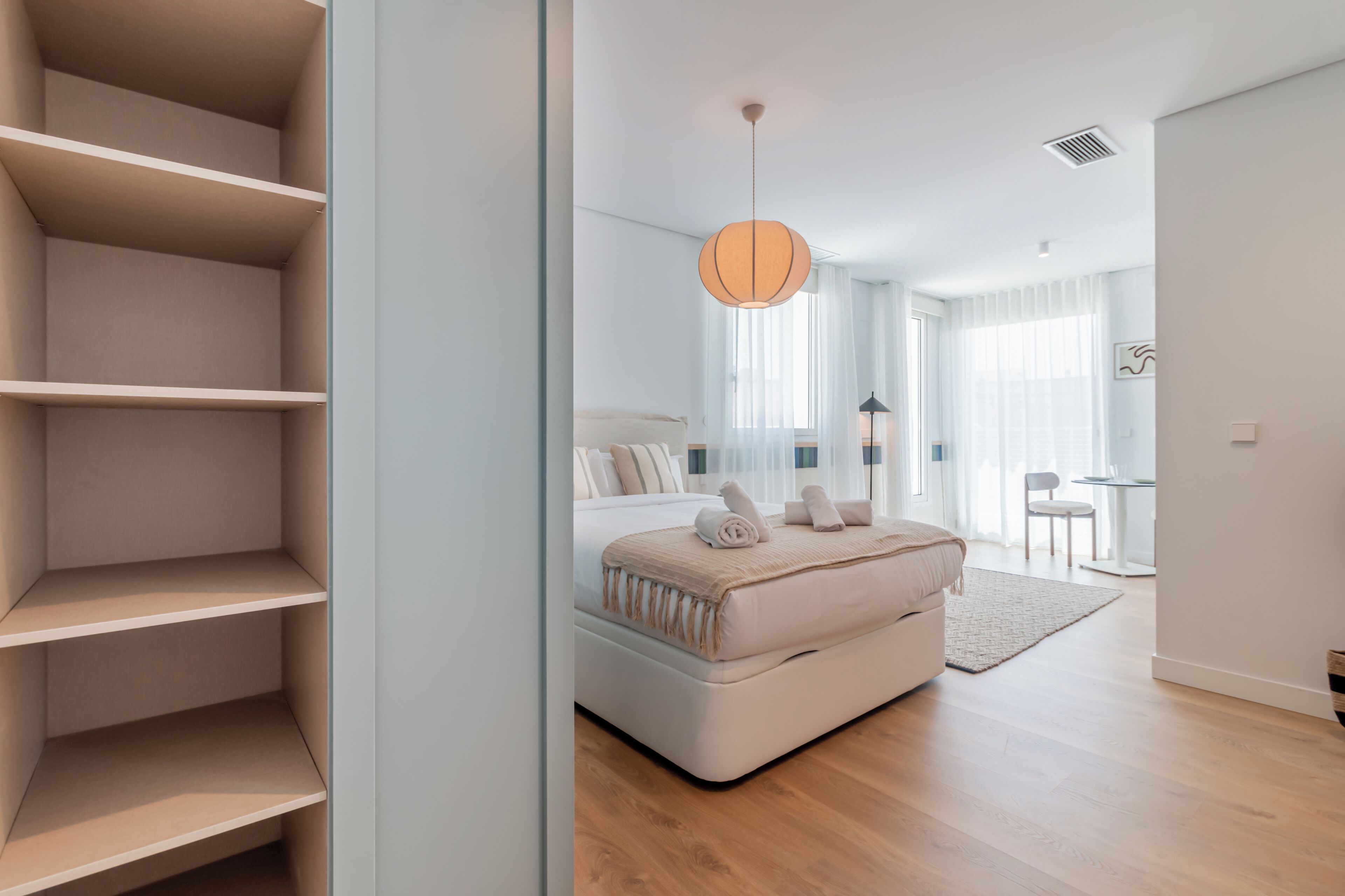 Un dormitorio moderno con una cama, un ventanal grande y un mueble de almacenamiento empotrado.