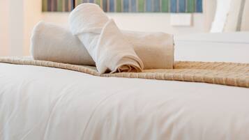 A neatly made bed with a rolled towel, a black floor lamp, and a striped wall decoration.