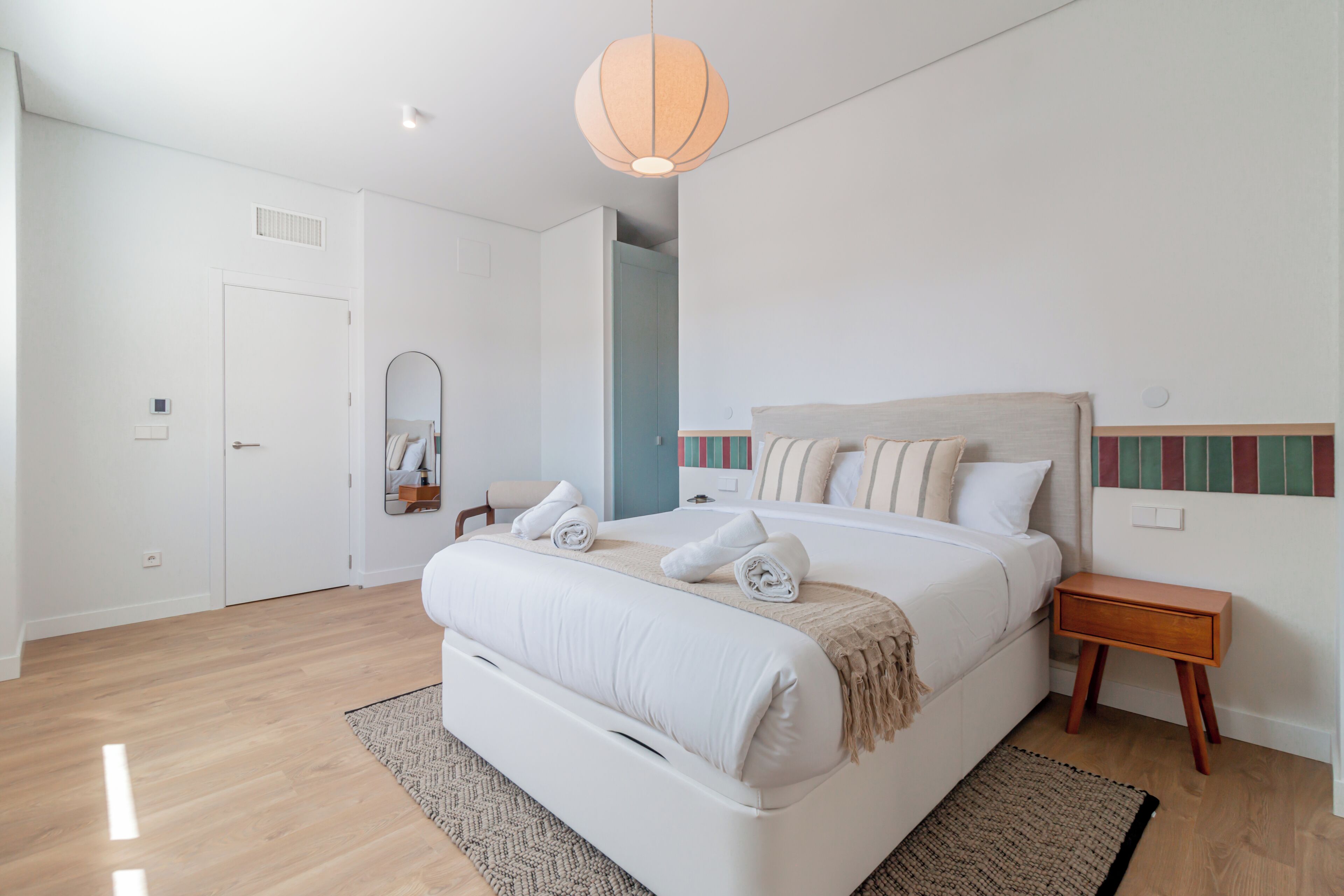 A bedroom with a bed, bedside table, and a hanging light fixture.