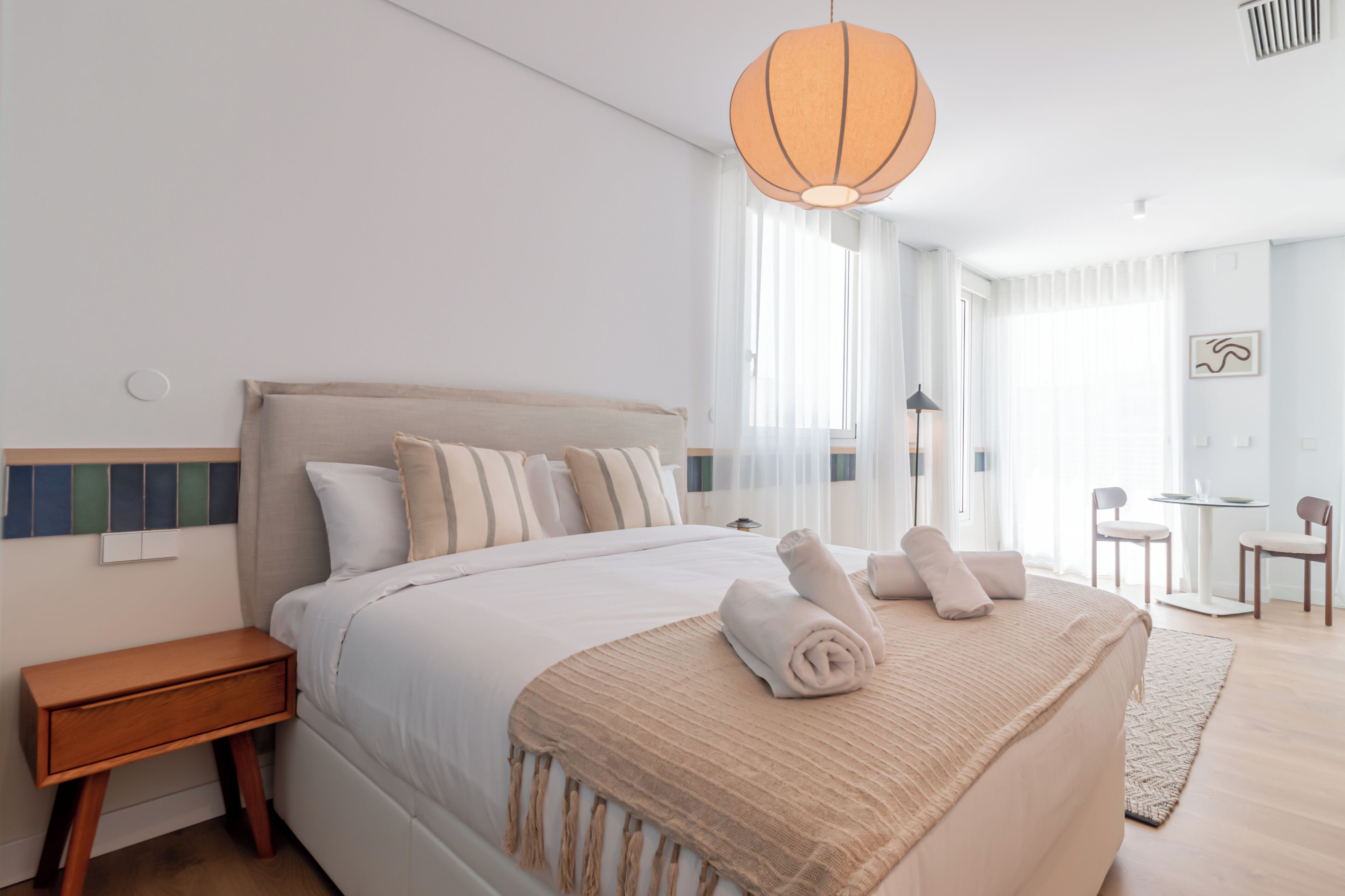 A modern hotel room with a large bed, a bedside table, a lamp, and a view of the room.