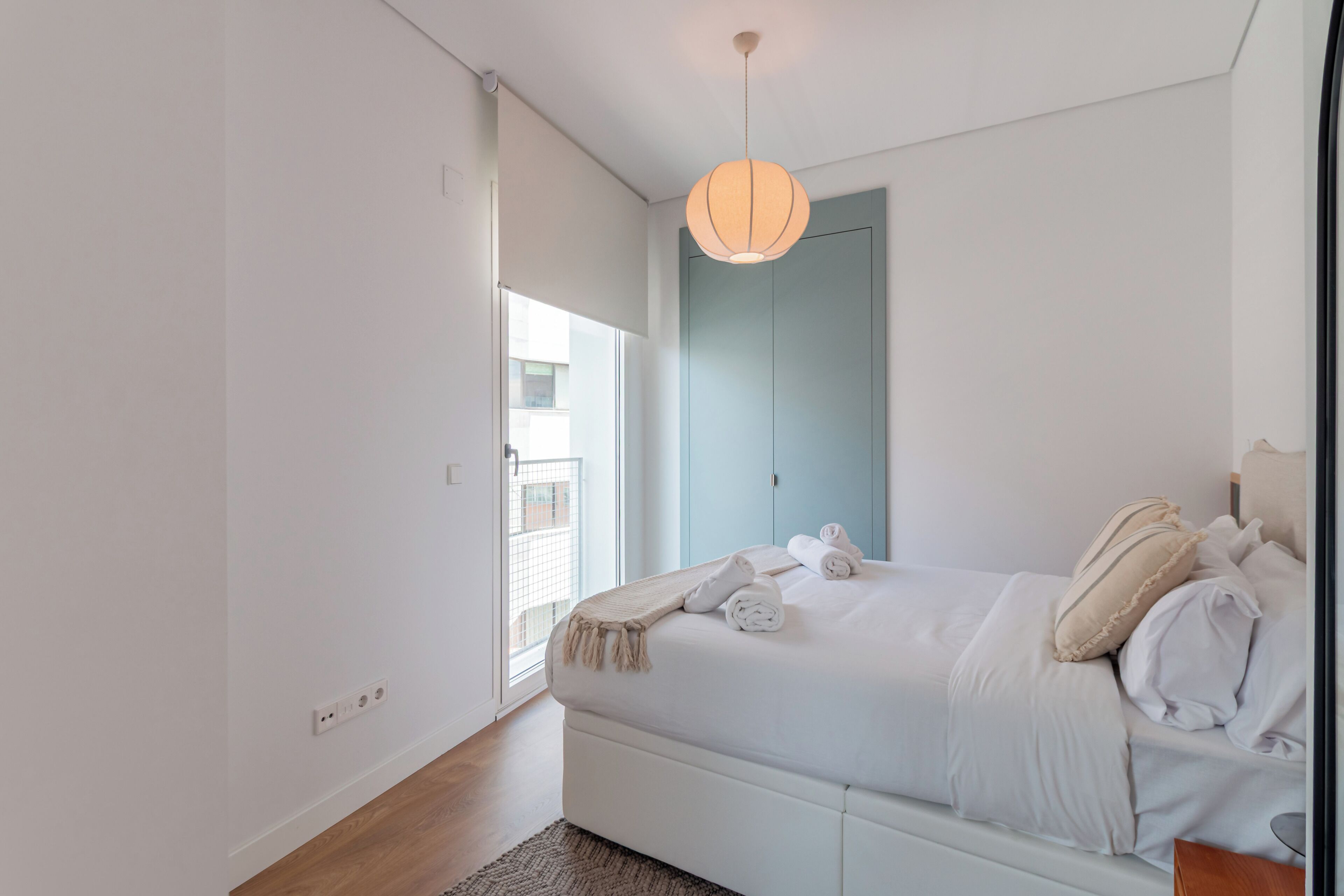 Een moderne slaapkamer met een bed, een hanglamp, een raam en een deur.