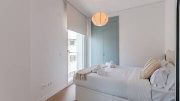 Een moderne slaapkamer met een bed, een hanglamp, een raam en een deur.