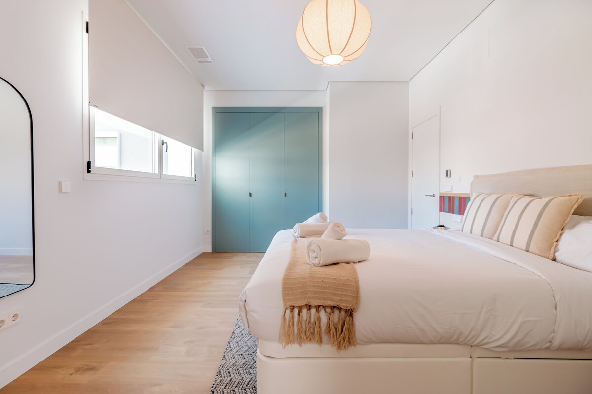 Un dormitorio moderno con una cama grande, una puerta azul y una lámpara colgante.
