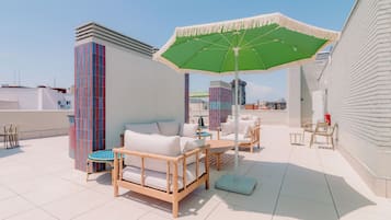 Een dakterras met tuinmeubilair, een groene parasol en uitzicht op de stad.