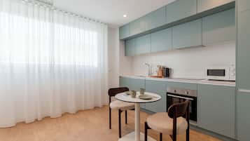 Een moderne keuken met lichtblauwe kastjes, een ronde eettafel met stoelen en een raam met dunne gordijnen.