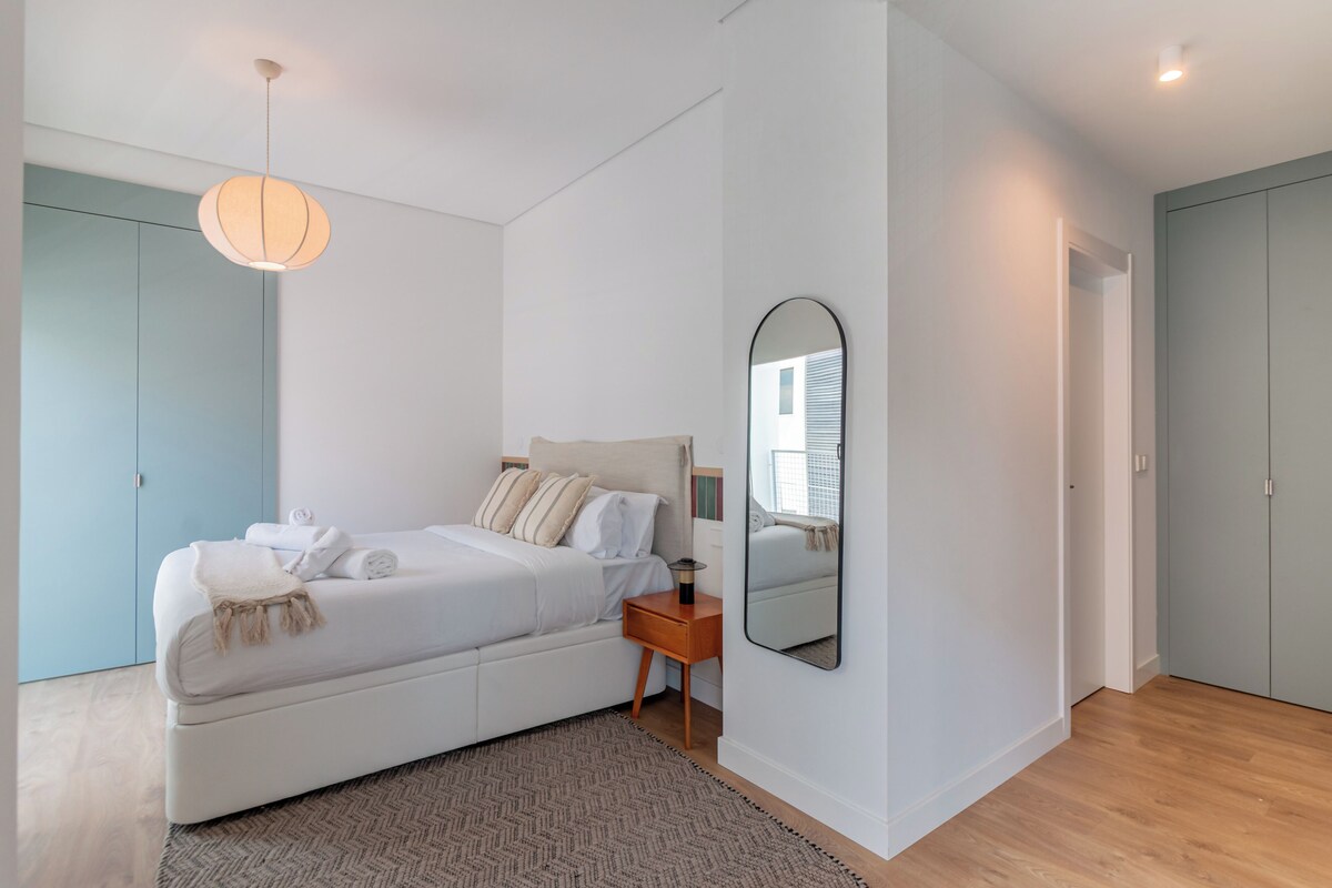 Un dormitorio con cama, mesita de noche, lámpara y espejo en la pared.
