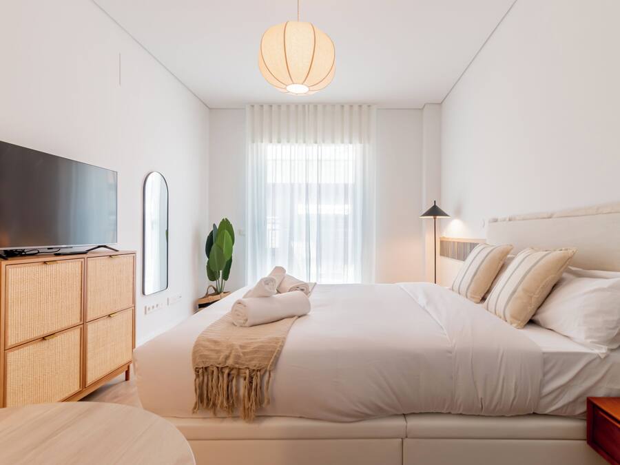 A bedroom with a bed, a TV, a bedside table, a lamp, and a window with curtains.