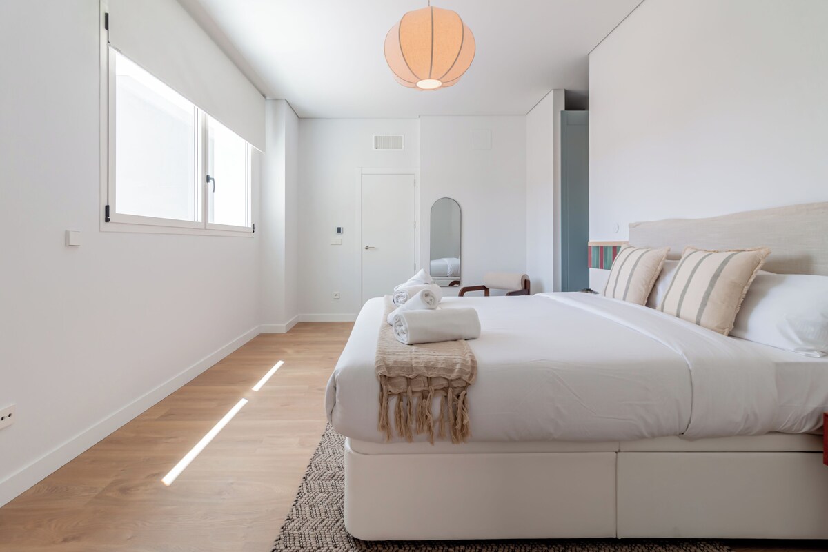 Un dormitorio moderno con una cama grande, una mesita de noche, un espejo y una ventana.