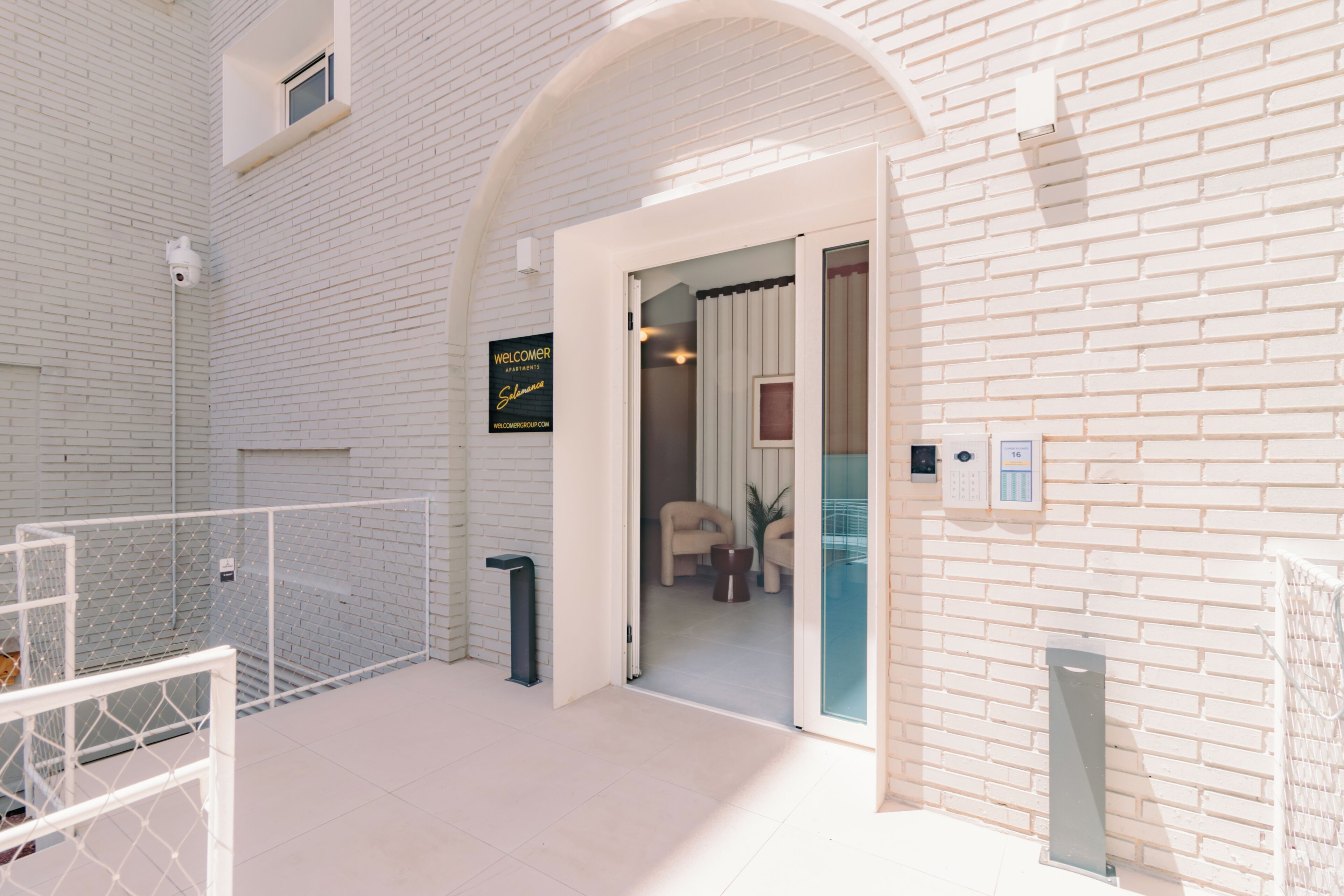 Un interior moderno con paredes de ladrillo blanco, una entrada con puerta de cristal y una habitación visible con muebles.