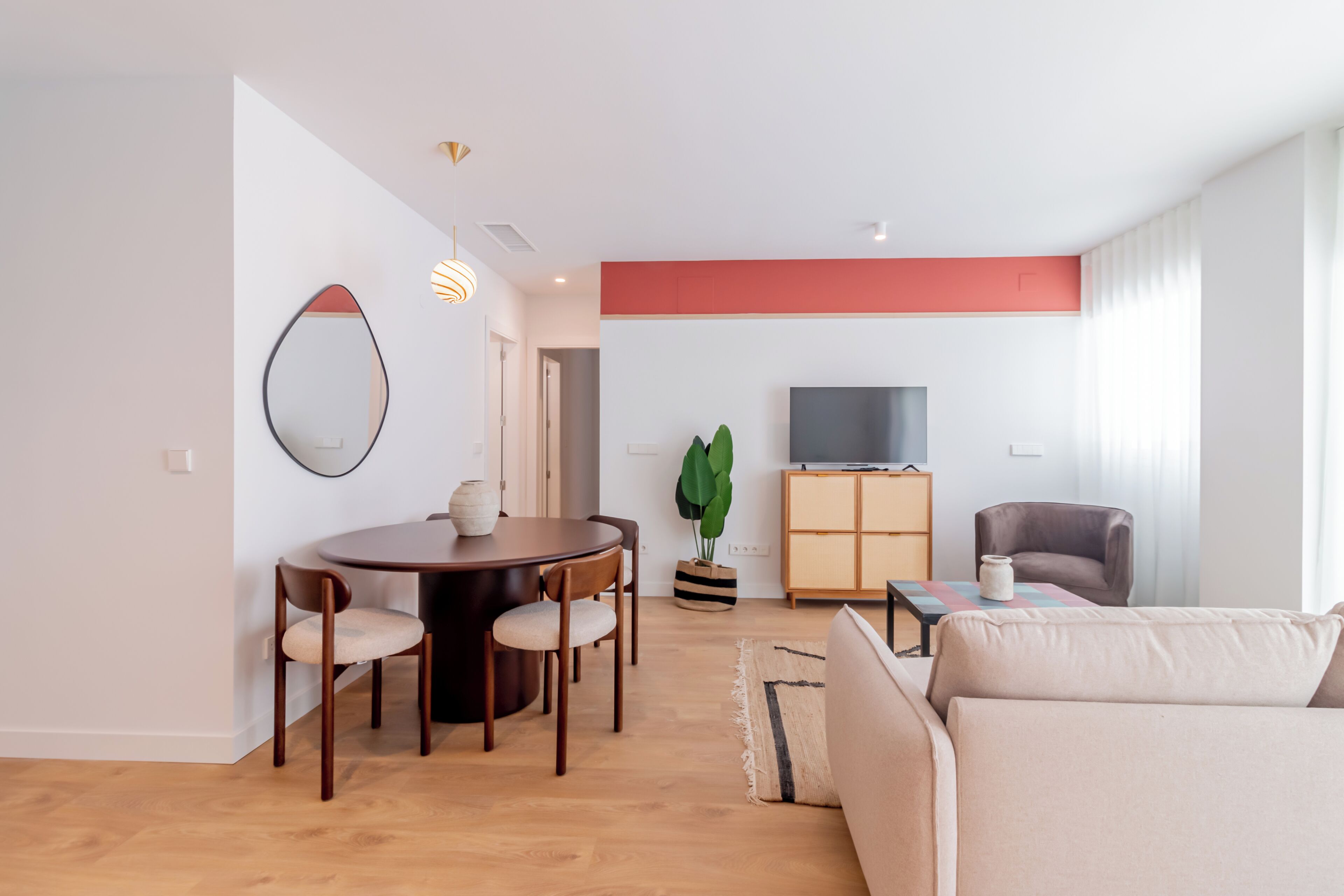 A modern living room with a dining area, a sofa, a TV, and a plant.