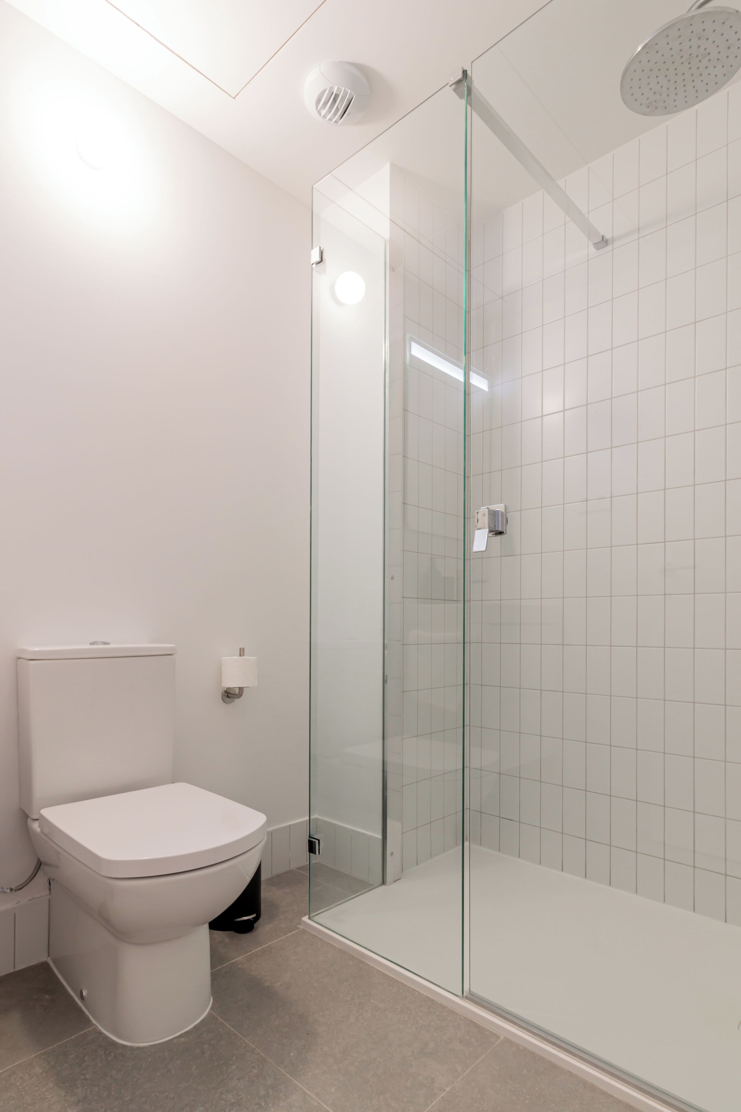 A modern bathroom with a toilet, a glass shower enclosure, and a tiled wall.