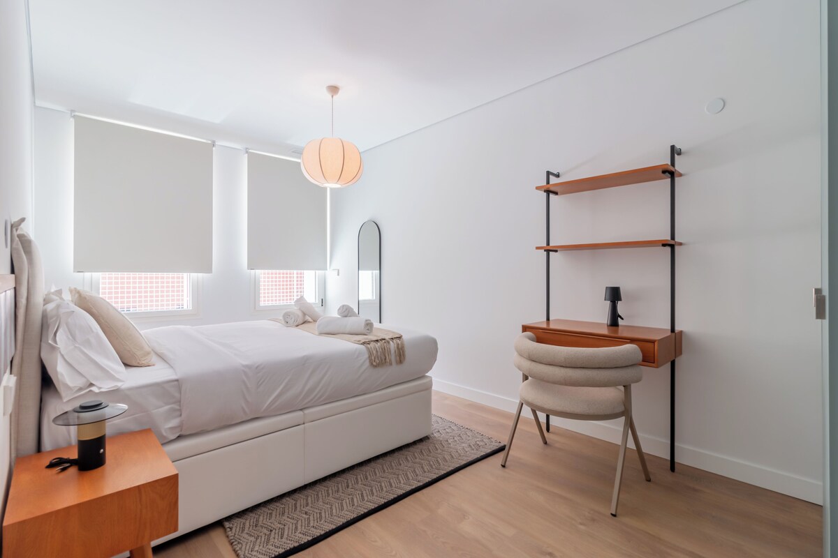 Un dormitorio moderno con cama, mesita de noche, silla y estante en la pared.
