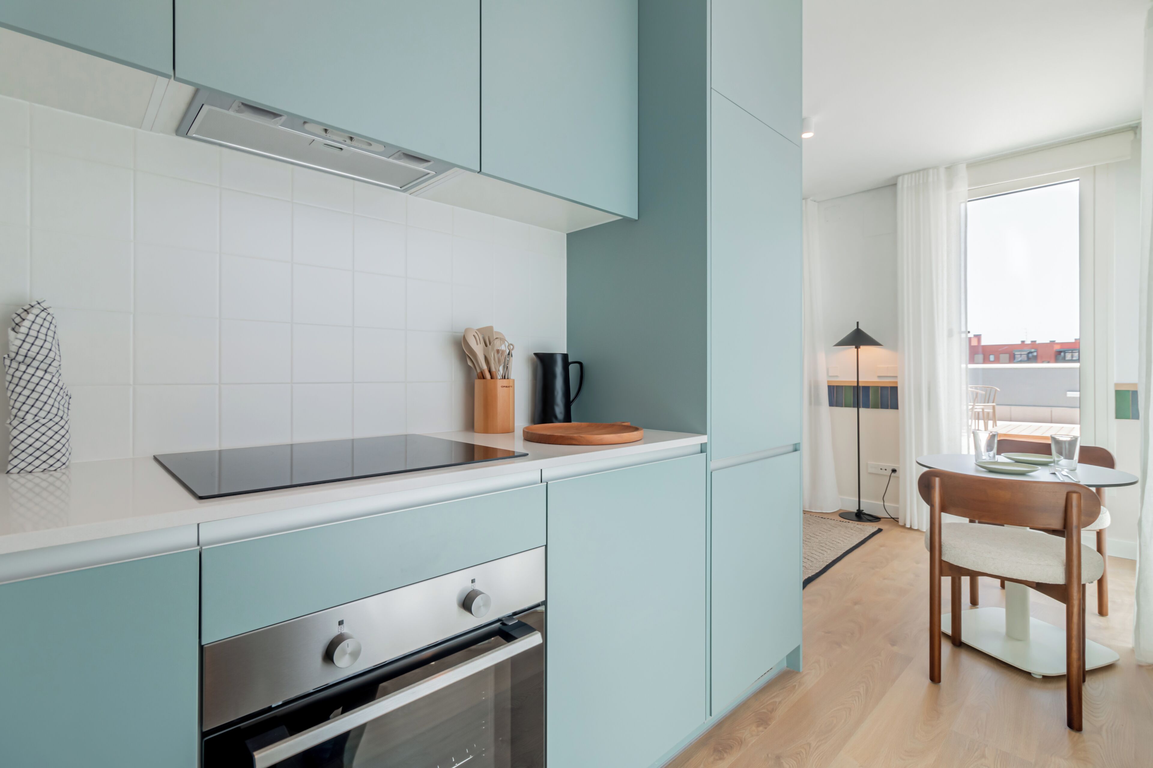 Une cuisine moderne avec des meubles de couleur bleu clair, une plaque de cuisson à induction noire et une planche à découper en bois.