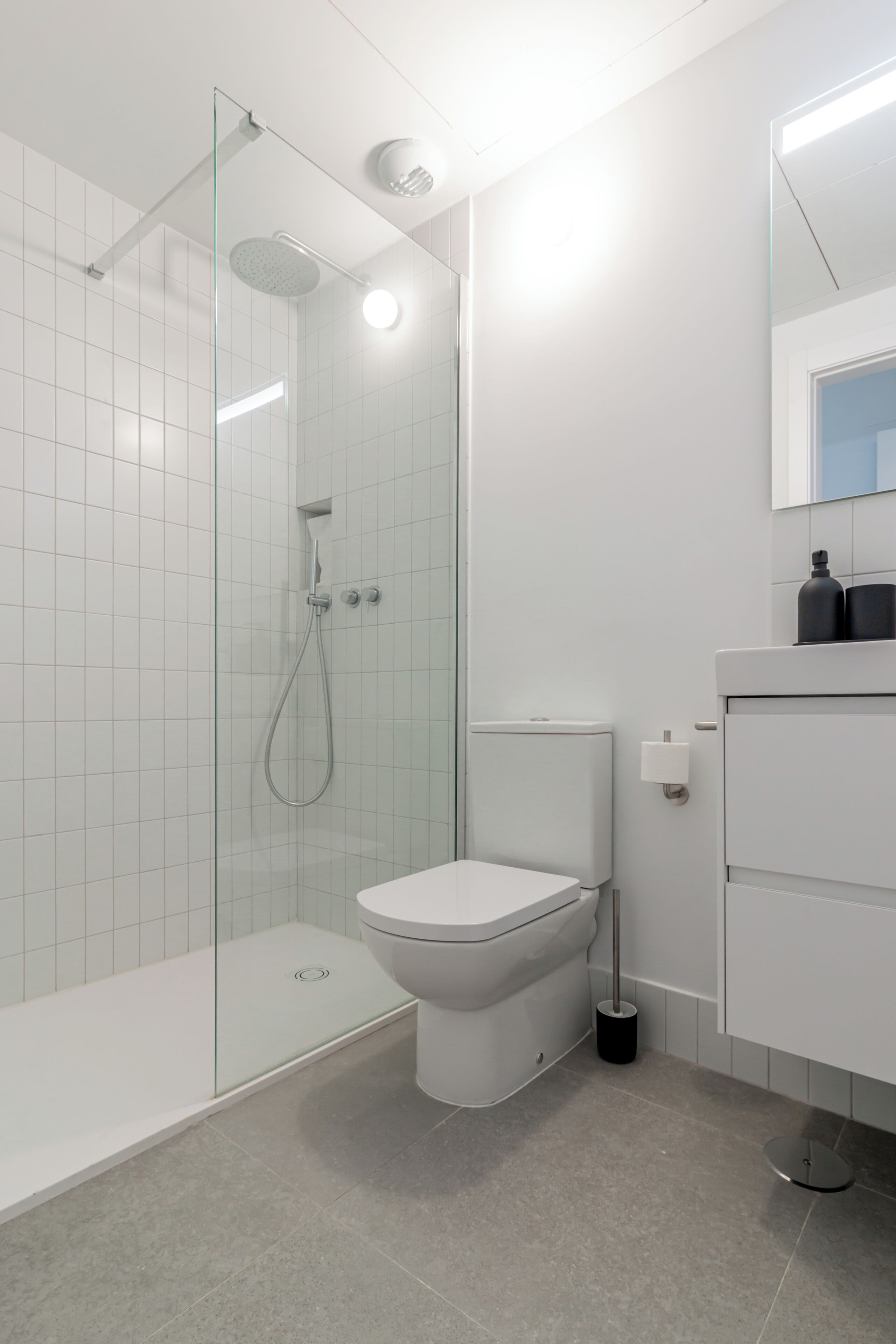 A modern bathroom with a glass-enclosed shower, a toilet, and a sink with a mirror above.