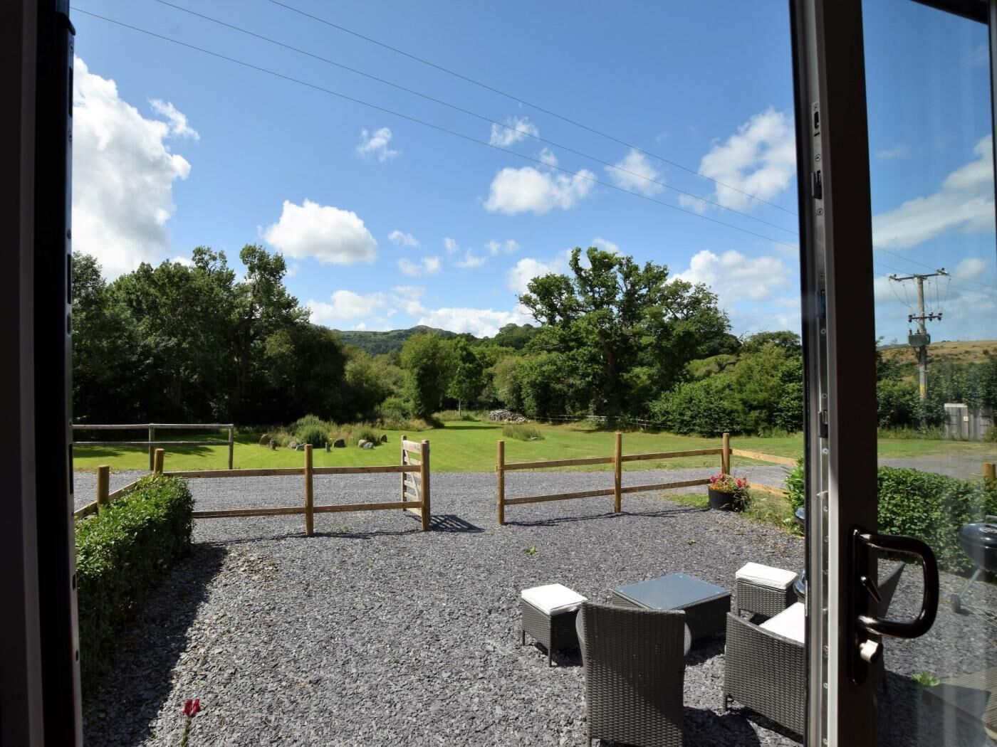 A view through a glass door of a patio area with outdoor seating and a gravel path.