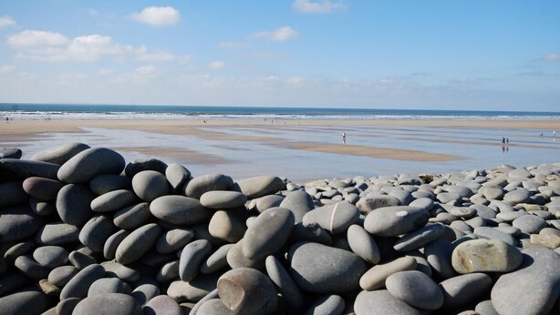 A beach with large rocks in the foreground and a sandy shore with people in the background. - 2 Bed in Bideford (oc-60428) (Pusehill)