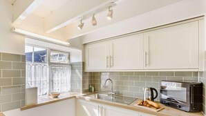 A modern kitchen with white cabinets, a built-in oven, and a window with curtains. - 2 Bed in Bideford (oc-60428) (Pusehill)