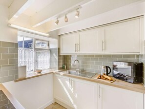 A modern kitchen with white cabinets, a built-in oven, and a window with curtains. - 2 Bed in Bideford (oc-60428) (Pusehill)