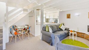 A modern living room with a grey sofa, colorful chairs, a dining table, and a kitchen in the background. - 2 Bed in Bideford (oc-60428) (Pusehill)
