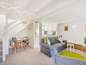 A modern living room with a grey sofa, colorful chairs, a dining table, and a kitchen in the background. - 2 Bed in Bideford (oc-60428) (Pusehill)