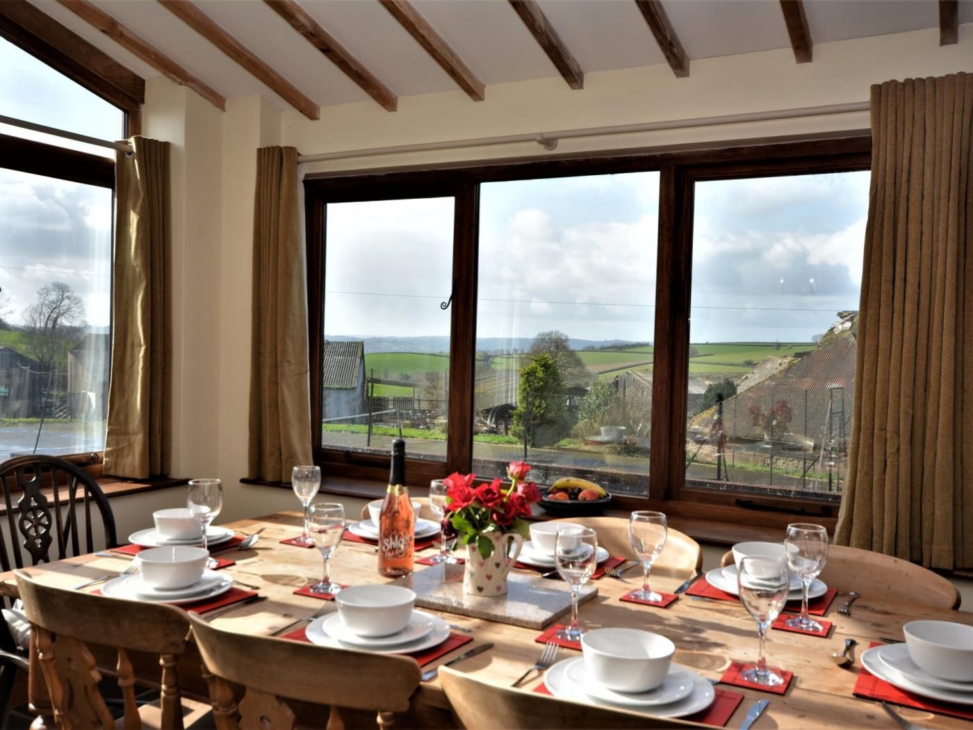 A dining table set for four with a view of the countryside through large windows.