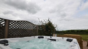 Ein Whirlpool mit Wasserstrahlen, umgeben von einem Holzzaun und einer Holzbank, mit bewölktem Himmel im Hintergrund.