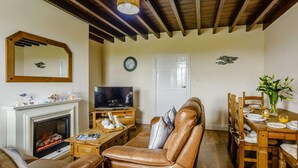 A living room with a fireplace, leather sofa, wooden dining table, and a television. - 2 Bed in Alnwick (oc-60464) (Boulmer)