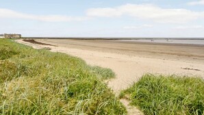 A beach with a sandy shore, grassy dunes, and a distant view of the sea. - 2 Bed in Alnwick (oc-60464) (Boulmer)