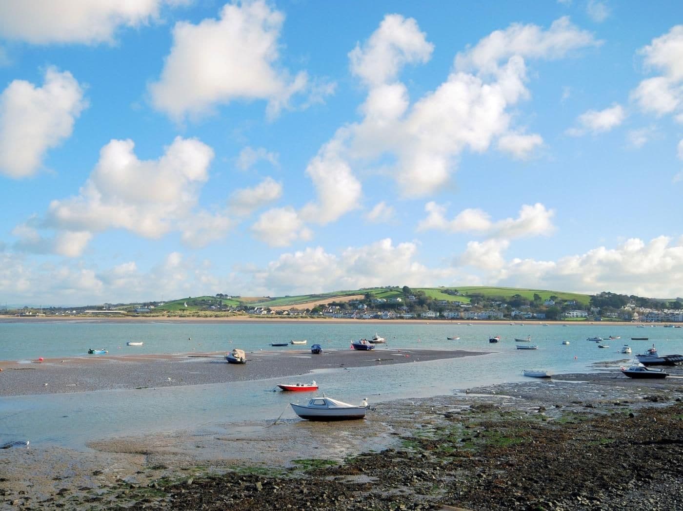 A coastal landscape with boats on a sandy beach and a town in the distance.