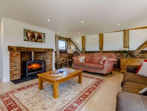 A cozy living room with a fireplace, a striped sofa, a wooden coffee table, and a patterned rug. - 4 Bed in Gloucester (oc-60200) (Redmarley D'Abitot)
