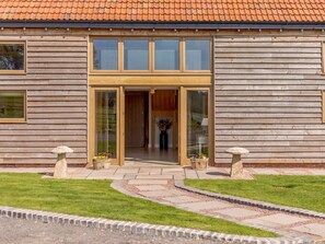 A wooden building with a tiled roof, large glass doors, and a paved entrance area with two stone planters. - 4 Bed in Gloucester (oc-60200) (Redmarley D'Abitot)