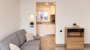 Una sala de estar moderna con un sofá gris, una mesita de madera y una cocina al fondo.