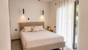 Un dormitorio moderno con una cama grande, una mesita de noche, una lámpara de pared y una ventana con cortinas.