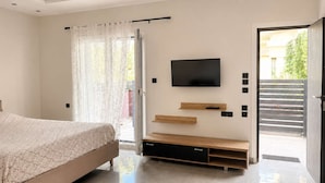 Un dormitorio moderno con cama, televisor montado en la pared y puerta corredera que da a un espacio exterior.