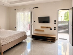 Ein modernes Schlafzimmer mit einem Bett, einem an der Wand befestigten Fernseher und einer Schiebetür zu einem Außenbereich.