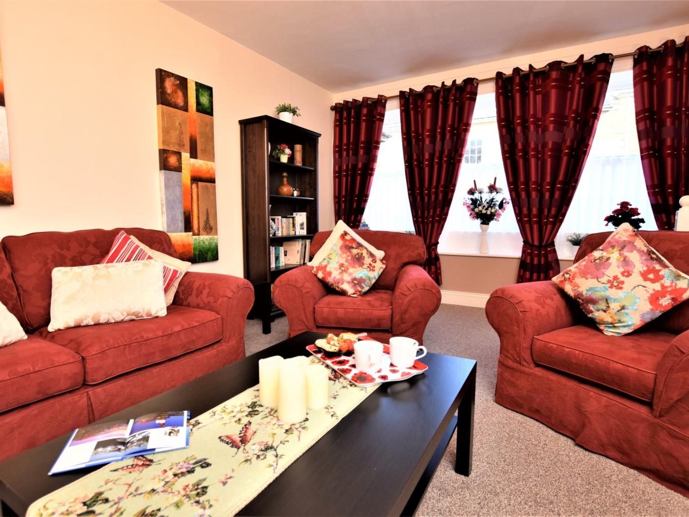 A living room with two red sofas, a coffee table, a bookshelf, and a window with curtains.