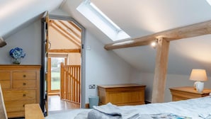 Une chambre avec une lucarne, des poutres en bois, un lit avec des serviettes, une table de chevet et une commode.
