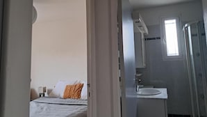 Hotelkamer met een bed, nachtkastje, raam, badkamer met wastafel en spiegel, en douche.