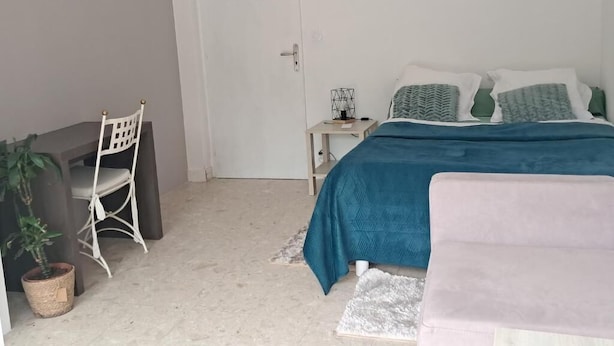 Een slaapkamer met een bed, een bureau, een stoel en een plant in een pot.