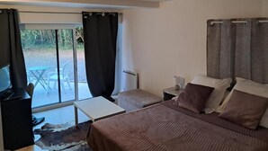Une chambre à coucher avec un lit, une télévision, une petite table et une vue sur l’extérieur grâce à une porte vitrée.