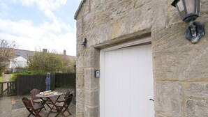 Un edificio de piedra con una puerta de garaje blanca, una mesa redonda con sillas y un farol de metal.