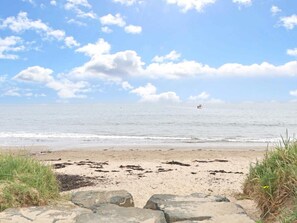Een strand met een heldere lucht, golven en een boot in de verte.