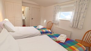 Un dormitorio con dos camas, una ventana con cortinas, un radiador y una puerta que da a un baño.
