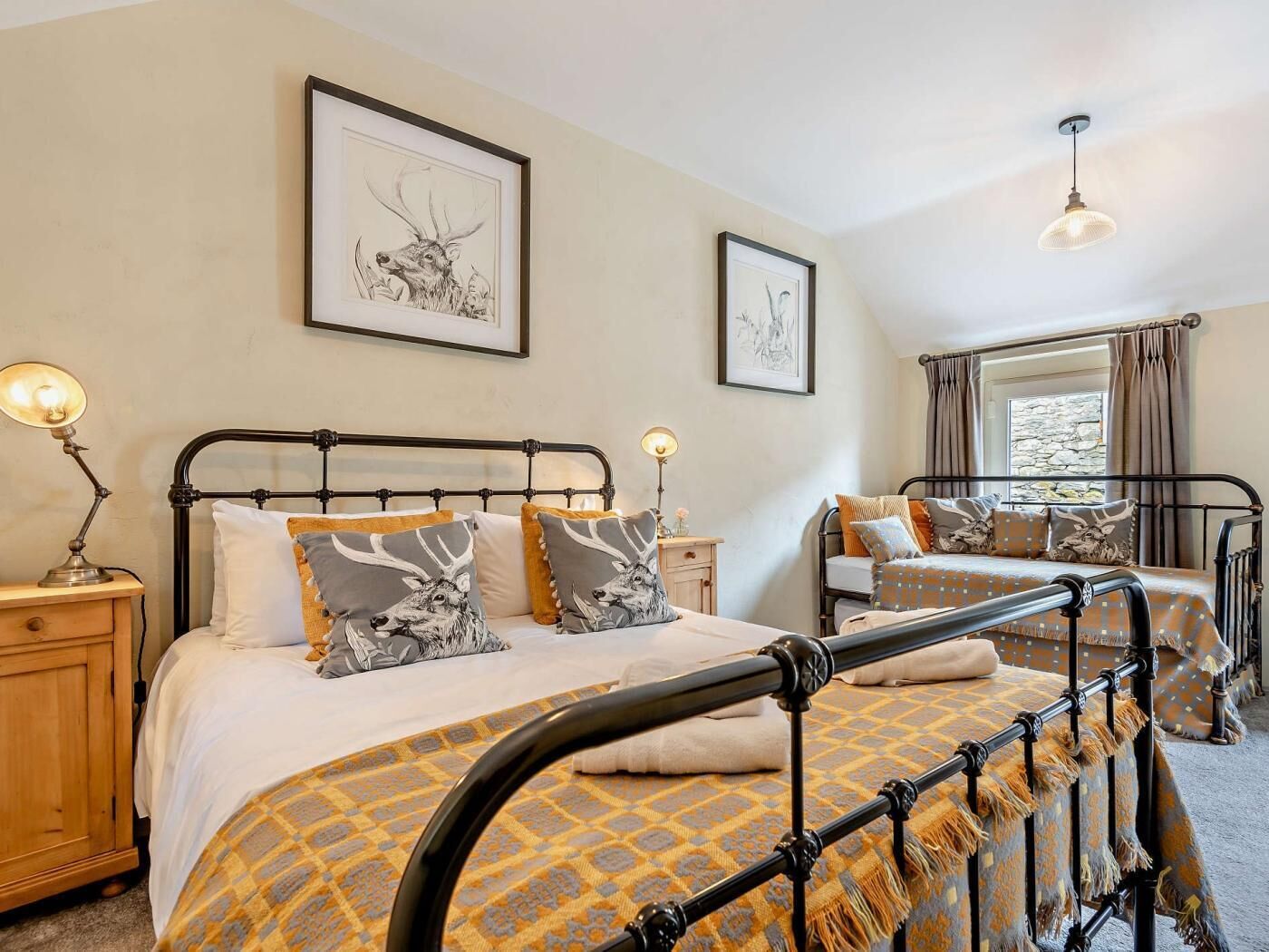 A bedroom with two beds, a nightstand with a lamp, and framed artwork on the walls.