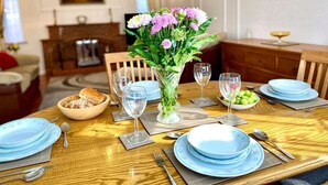 Ein Esstisch ist mit blauen Tellern, Besteck und Weingläsern gedeckt, in der Mitte steht eine Blumenvase.