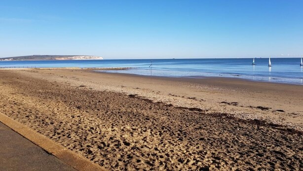 Ein Strand mit blauem Himmel, sandigem Ufer und einer fernen Küste.