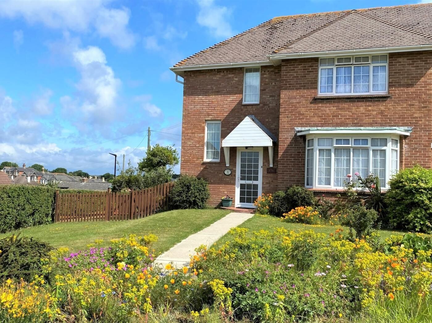 A two-story brick house with a front garden, a visible front door, and a small pathway leading to the entrance.