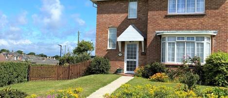 A two-story brick house with a front garden, a visible front door, and a small pathway leading to the entrance.