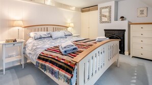 Um quarto com cama, mesas de cabeceira, cômoda, espelho e lareira.